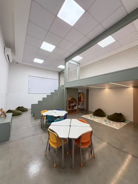 Sala infantil com mesas coloridas, pufes e mezanino com rede de proteção